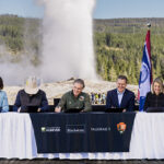 Five fund partners seated at the signing table for the Conservation and Stewardship Fund, with Old Faithful erupting behind them. Photo by the National Park Service.